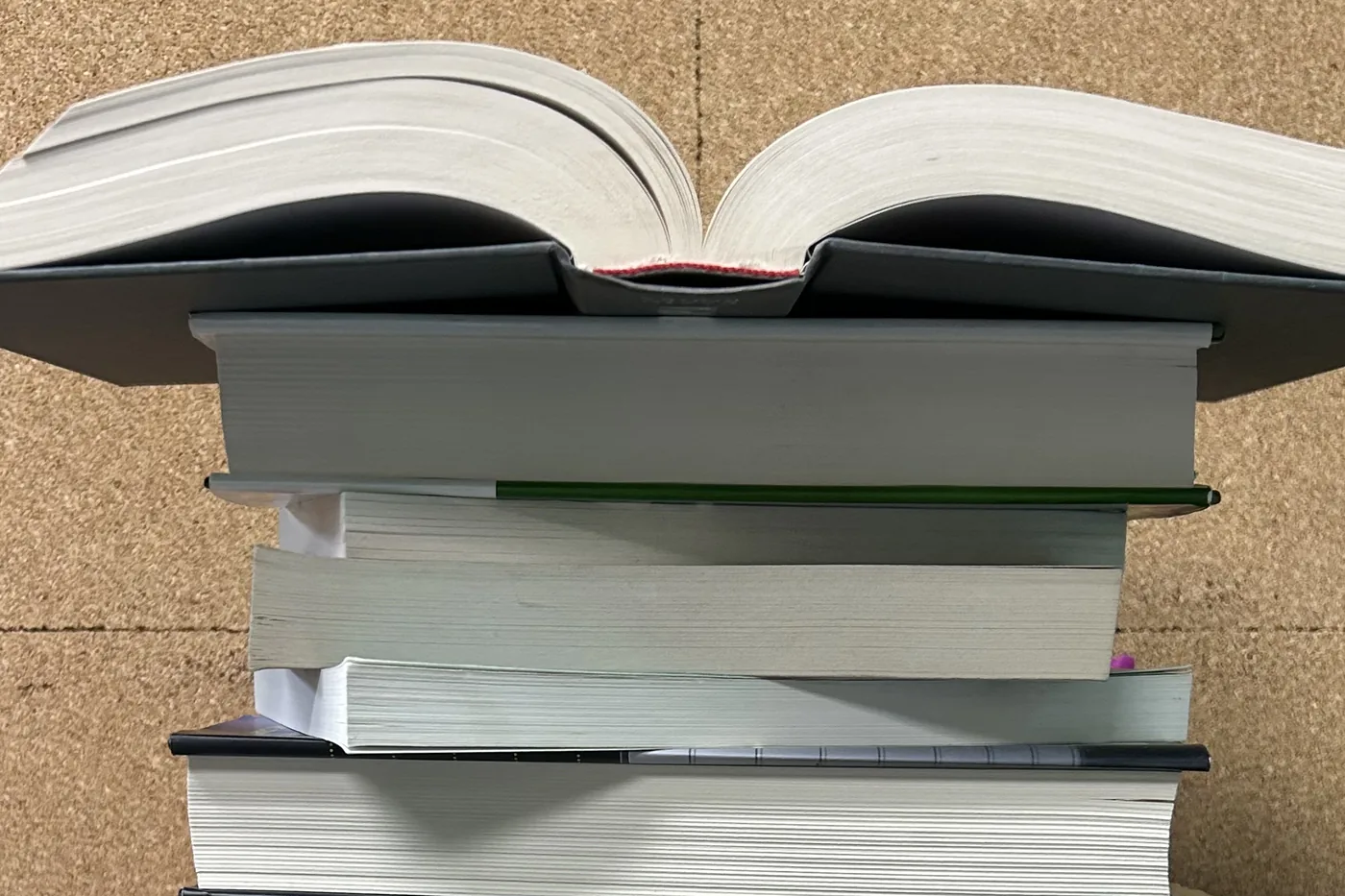 An open book resting atop a tall stack of reference works and research volumes