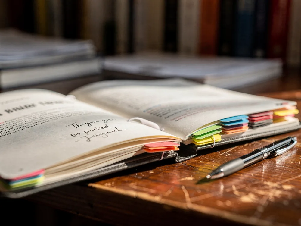An open proposal folder with tabbed sections on an editor's desk